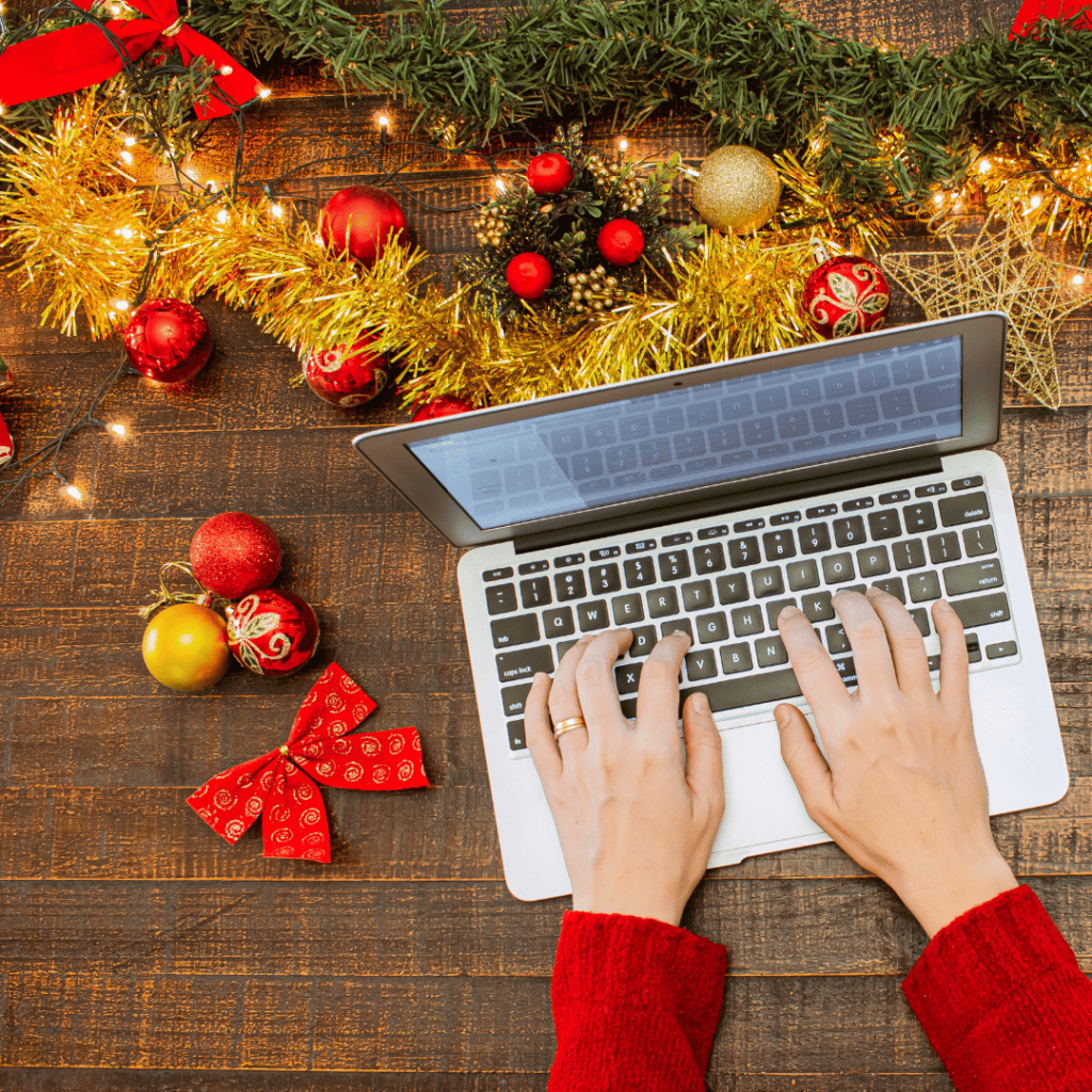 Hands typing on a laptop keyboard with holiday decor around.